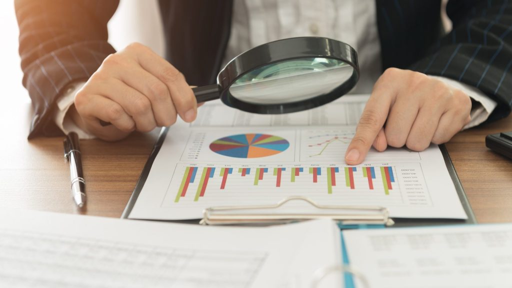 Un professionnel en chemise blanche examine des graphiques financiers sur des documents papier avec une tablette électronique à portée de main
